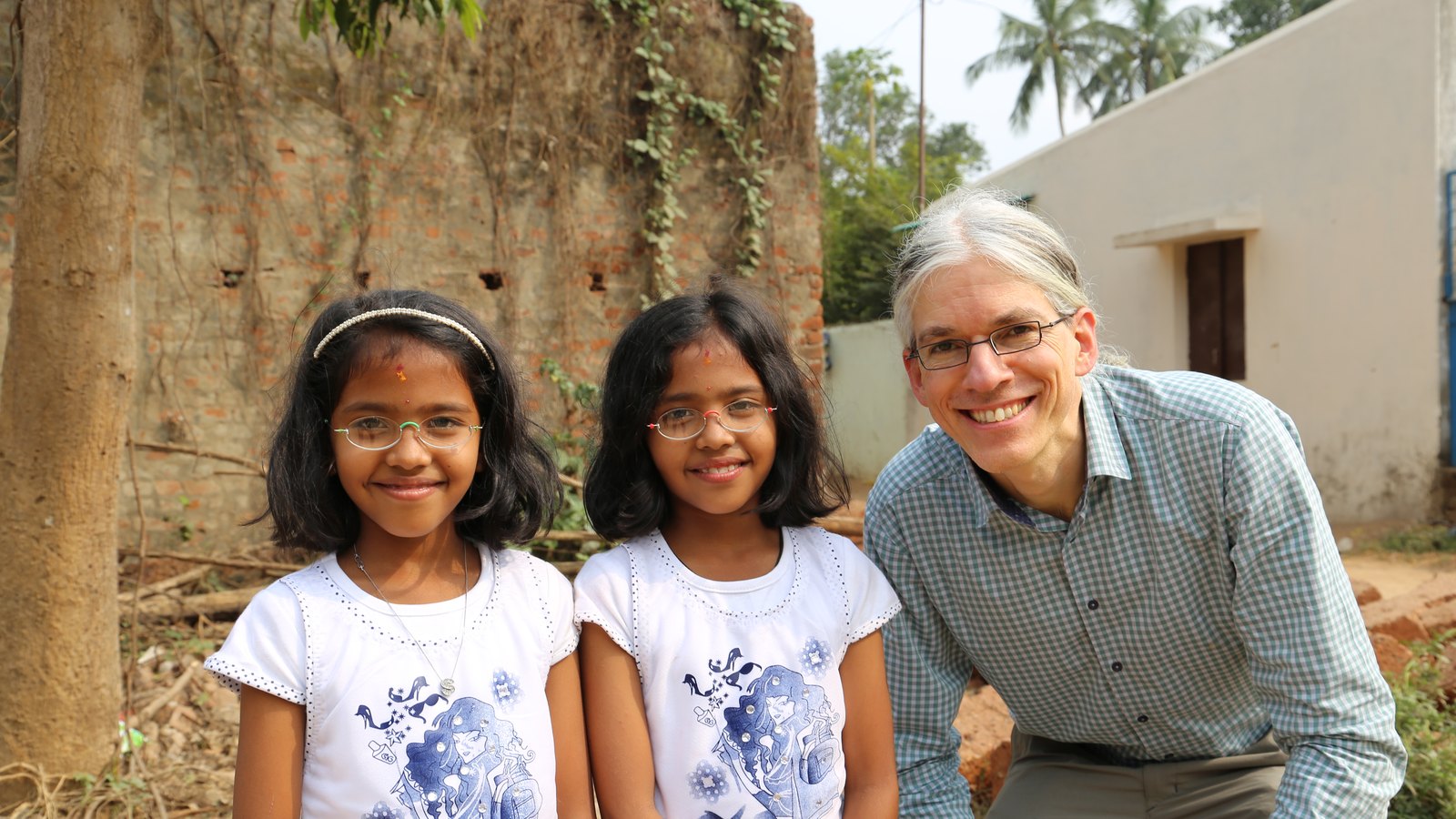 Zwei Mädchen mit Brillen von EinDollarBrille stehen neben einem Mitarbeiter der Organisation, aufgenommen in Indien
